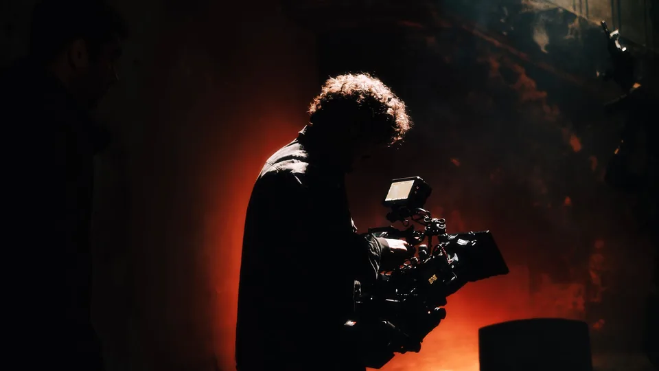 A camera operator silhouetted against a lit set
